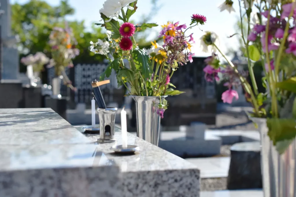 Vases de fleurs et bougies déposés sur une pierre tombale dans un cimetière.